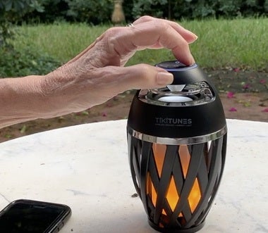 Illuminated TikiTunes speaker on a patio table with a hand operating its top control